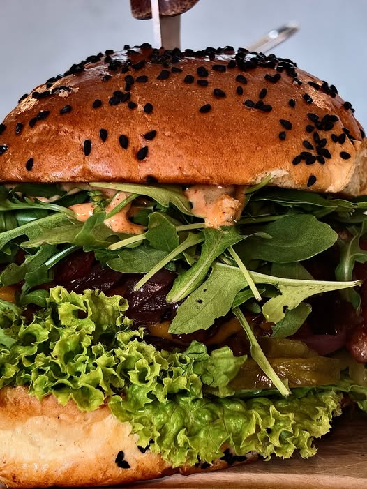 Zbliżenie na burgera z sezamem czarnuszkowym, rukolą i sosem